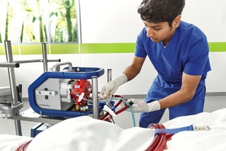 Healthcare professional in blue scrubs adjusting medical equipment beside a patient in a hospital setting.