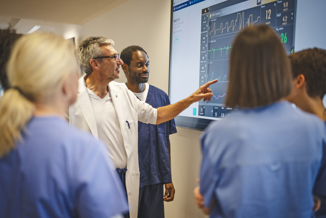 Servo wall-display screen in training environment with doctor pointing at screen niv nava with five clinicians