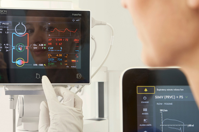 A healthcare professional interacts with a medical monitor displaying patient vital signs and several data graphs.