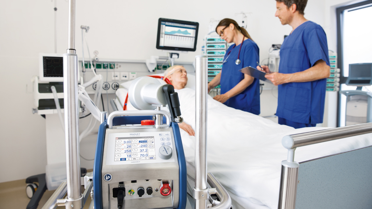 Medical staff in blue scrubs attend to a patient in a hospital bed, with medical equipment in the foreground.