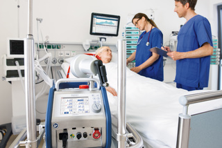 Medical staff in blue scrubs attend to a patient in a hospital bed, with medical equipment in the foreground.