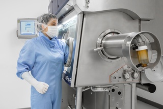 A lab technician in blue protective gear operates a machine in a clean room.