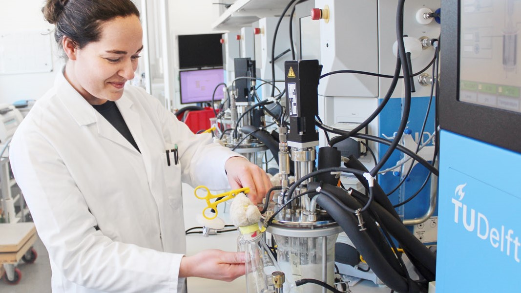 A scientist in a lab coat works with complex laboratory equipment at TU Delft.