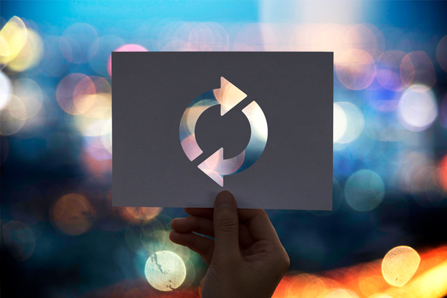 Hand holding paper with circular refresh cutout against blurred colorful bokeh lights background.