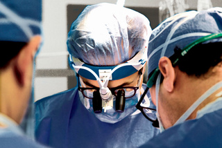 Surgeons in blue scrubs and masks focus intently during a surgical procedure in an operating room.