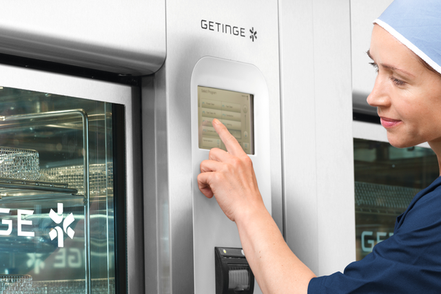 A healthcare worker in a blue uniform operates a medical sterilization machine.